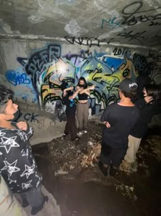 some people are standing in a tunnel with graffiti on the wall and one person is pointing at something