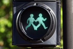 a green pedestrian crossing signal with two people walking on the crosswalks and trees in the background