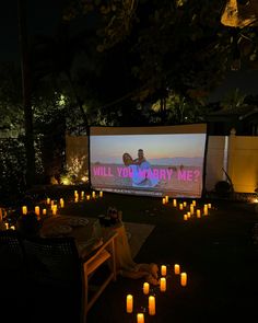 an outdoor movie screen is lit up with candles in front of it and the words will you marry me?