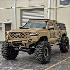 a yellow truck parked in front of a building with large tires on it's sides