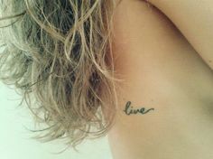 the back of a woman's neck with a small tattoo that says live on it