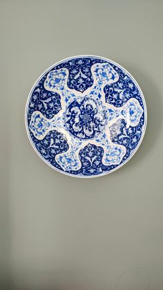 a blue and white plate sitting on top of a gray wall next to a clock