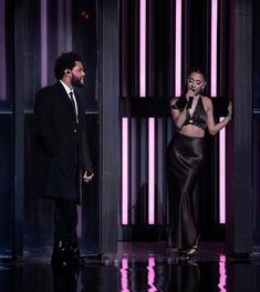 lady in black dress standing next to man on stage