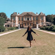 a woman standing in front of a large building on top of a lush green field