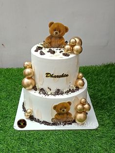 a three tiered cake decorated with gold balls and a teddy bear sitting on top