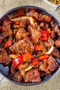 meat and vegetables in a pan with spoons next to it on a tablecloth