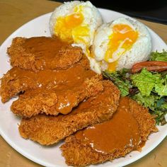 fried chicken with gravy, rice and salad on a white plate next to two eggs