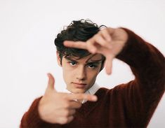 a young man is pointing his finger at the camera while wearing a brown sweater and white shirt