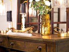 a gold vase with white flowers sitting on top of a wooden table next to a mirror