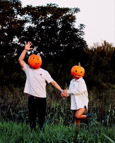 two people holding hands with pumpkins on their heads in the middle of a field