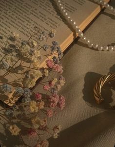 an open book with pearls and flowers next to it