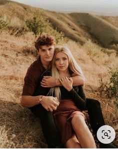 a man and woman sitting on top of a hill