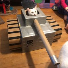 a white cat sitting in a tank made out of cardboard on top of a wooden floor