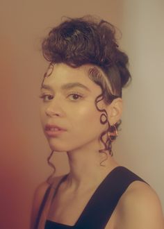 a woman with curly hair wearing earrings and a black dress looking off to the side