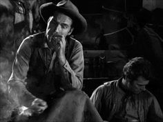 black and white photo of two men sitting next to each other, one with his hand on his face