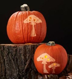 two carved pumpkins sitting on top of a tree stump with mushrooms painted on them