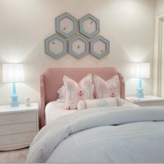 a bed with pink and blue pillows on top of it next to two nightstands