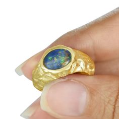 a hand holding a gold ring with a blue opal stone in it's center