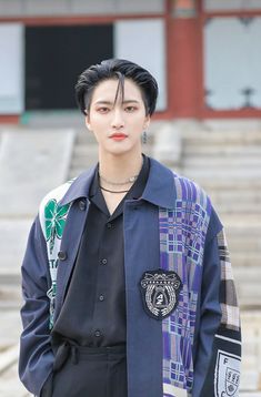 a man with black hair wearing a blue jacket and tie standing in front of some steps