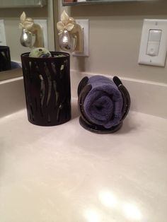 a bathroom sink with a purple towel on the edge and a black cup next to it