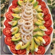 a platter filled with sliced tomatoes, avocado and onion on top of a checkered table cloth