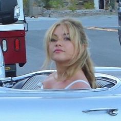 a woman sitting in the driver's seat of a white car with her eyes closed