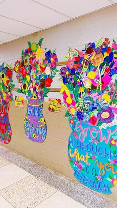 three vases with flowers are on the wall in front of a school hallway mural