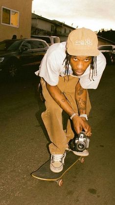 a young man riding a skateboard down a street next to a parked car and holding a camera