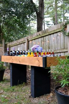 an outdoor table with bottles on it in the grass next to a fence and potted plants