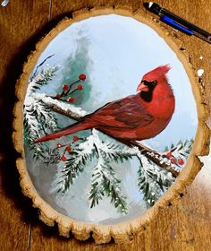 a red bird sitting on top of a tree stump next to snow covered pine branches