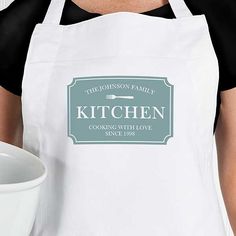 a woman holding a white apron with the words kitchen cooking with love since 1994 on it