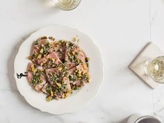 a white plate topped with meat and veggies next to two glasses of wine