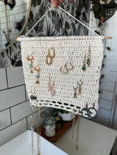 a white crocheted wall hanging with lots of earrings on it and a hand holding the hanger