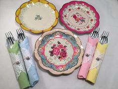 four plates, two forks and three napkins with flowers on them sitting next to each other