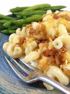 a blue plate topped with macaroni and cheese covered in sauce next to green beans