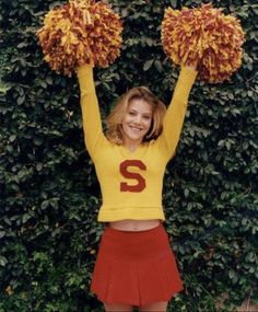 a woman in yellow and red cheerleader outfit holding two pom poms over her head