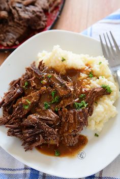 a white plate topped with meat and gravy on top of mashed potatoes