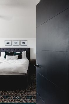 a white bed sitting next to a black door in a room with pictures on the wall