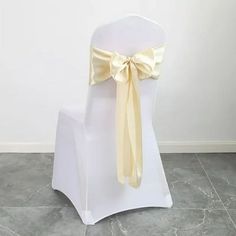 a white chair with a yellow bow on the back and seat cover is sitting in front of a wall