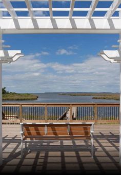 a wooden bench sitting under a white pergolated roof next to a body of water