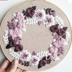 a hand is stitching a flowered heart on a hoop with white and purple flowers