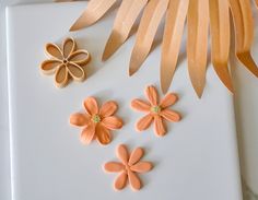 three flowers and two leaves on a white surface next to some brown paper strips that have been cut into flower shapes