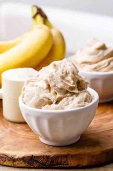 bananas and peanut butter in small white bowls on a wooden cutting board next to each other