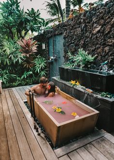 a woman laying in an outdoor bathtub with flowers on the floor and plants growing out of it