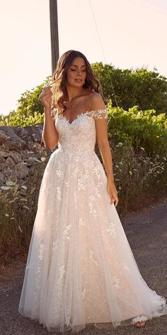 a woman in a wedding dress standing on the road with her hands behind her head