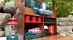 a wooden shelf filled with camping items next to some rocks and trees in the background