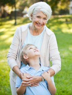 an older woman and young boy standing in the grass with their arms around each other