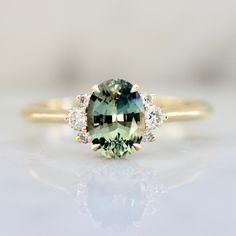 an oval cut green and white sapphire ring with three diamonds on the band, set in yellow gold