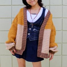 a woman standing in front of a white brick wall wearing a yellow and brown cardigan