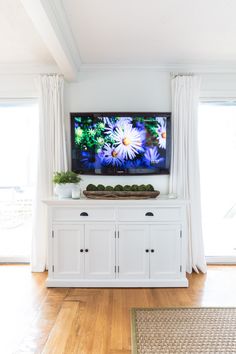 a flat screen tv sitting on top of a white cabinet in a living room next to a window